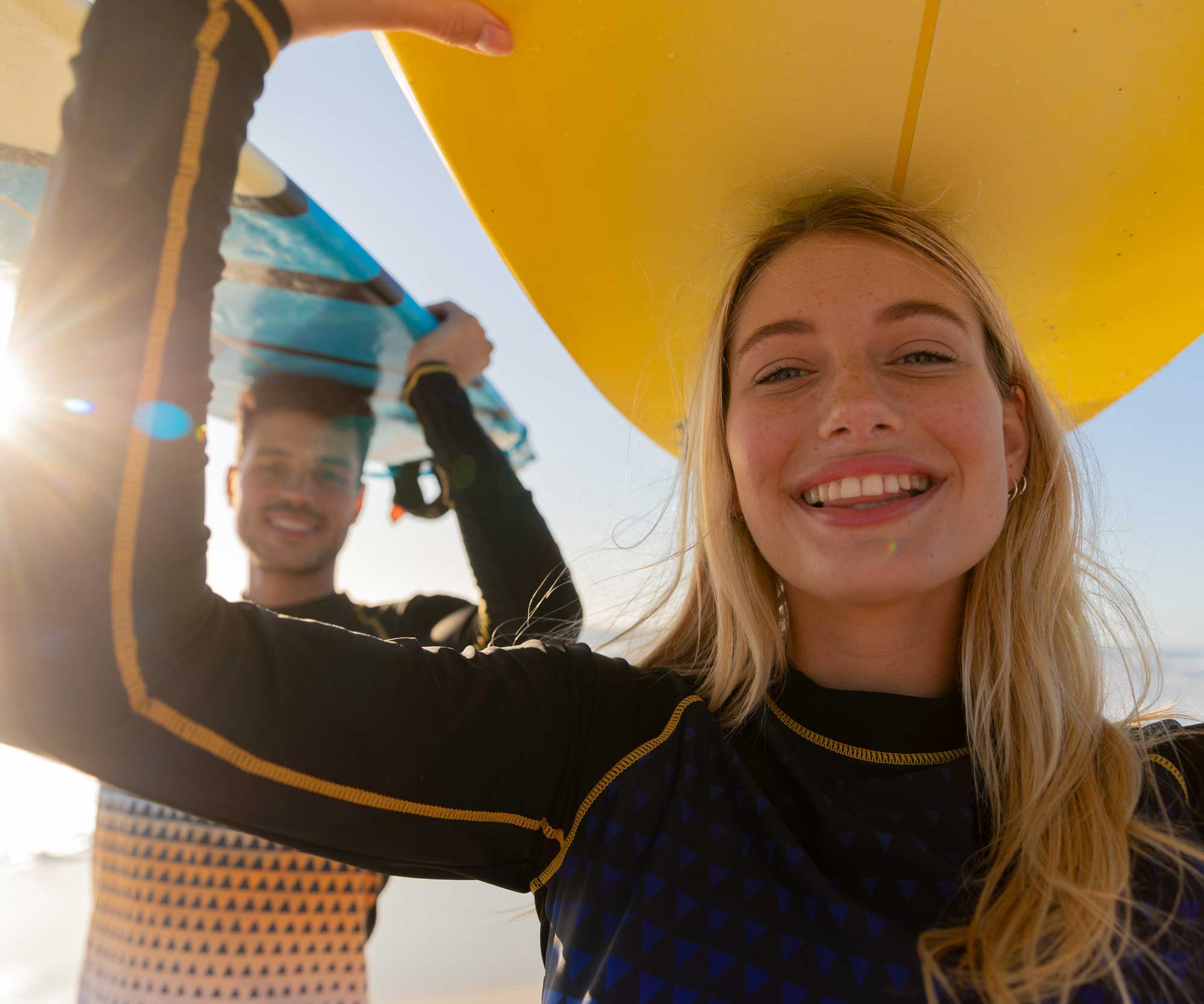 female and male surfer carrying surfboards on their heads